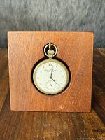 Antique pocket watch set in the wooden display stand on a wooden surface, clear view of all dial details.