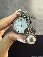Front view of antique pocket watch showing white dial and winding crown, attached to chain with silver fobs.