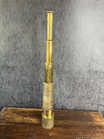 Telescope fully extended on wooden surface against grey backdrop.