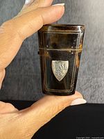 Front view of the antique etui case held by hand showing tortoiseshell body with sterling silver shield crest and delicate silver inlay borders.