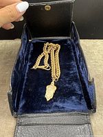 Gold-tone fob chain laid inside the open black leatherette case featuring a snap closure and blue velvet lining.