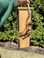 Full view of the carved cedar wine box holder showing its shape, strap and painted design.