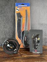 Photo showing all three items: Shimano fillet knife in packaging, Mitchell fishing reel, and Swiss Forge cutter boxed