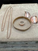 Five pieces of vintage Indigenous American jewelry including earrings, ring, chain necklace and wide bracelet/belt strap arranged on fabric background.