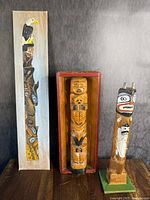 Group photo of three vintage Northwest Coast Indigenous artworks: a painted wooden panel totem, and two carved wooden totem poles.