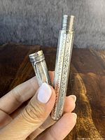 Close-up of the disassembled thermometer holder showing cap and main body with engraved designs and threaded end