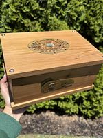 Photo of the top and front panel of the cedar box showing round carved and painted Indigenous artwork with abalone inlay on the lid.