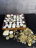 Wooden tray with over 40 white enamel dials surrounded by a loose pile of watch parts on a black surface