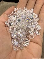 Hand holding a collection of clear faceted stones showing variety of shapes and sizes, highlighting sparkle and clarity.