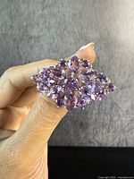 Front view of the large amethyst statement brooch showing faceted natural amethyst stones in sterling silver settings held by fingers on a black cloth background.