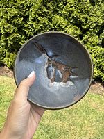 Front view of the conical form pottery bowl showing dark glaze with brown and blue abstract patterns.