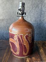 Front view of large reddish-brown pottery lamp with abstract cream design and metal lamp fixture on top.