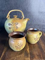 Set of pottery teapot with lid and handle, two cups with brown interiors, all with yellow speckled glaze and floral decoration