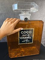 Front view with hand for scale showing large amber bottle with Chanel COCO Parfum label and seal on the neck