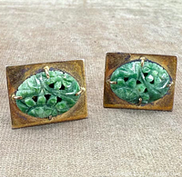 Pair of rectangular gold-tone cufflinks with carved green jade inserts resting flat on a fabric surface, showing tarnished metal and intricate jade carving.