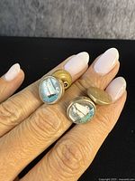 Pair of antique gold-tone Essex crystal cufflinks showing sailboat designs encased in round clear crystals, held between fingers.