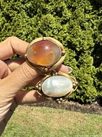 Photo showing both brooches held together, highlighting the color difference between agate and shell stones and the metal bead accents on the setting.