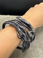 Photo of both black coral bangle bracelets worn on a wrist, showing their twisted and interwoven style and antique surface.