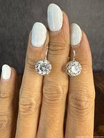 Pair of sterling silver hook earrings with large clear round stones, worn on fingers for scale and display.