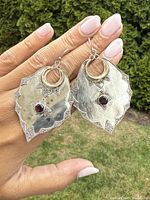 Photo showing both large vintage sterling silver earrings with gold crescent accents and natural garnet stones held in hand against a outdoor background.