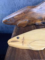 Close-up of abalone inlaid eyes on two salmon carvings, one dark stained and one light natural wood.