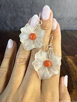 Front view of the pair of translucent flower-shaped earrings with natural coral centers, displayed on fingers showing size and detail.