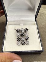 Close-up image of sterling silver floral pendant set with alternating clear and black stones in grid pattern inside jewelry box.