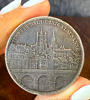Front side of coin medallion depicting Lausanne cityscape with 'FETE FEDERALE DE 1876 A LAUSANNE' inscription.