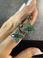 Photo of antique-style sterling silver drop earrings with star design accented with green marquise-shaped and red round stones, held by hand showing size and detail.