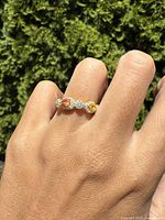 Photo showing the ring worn on a finger against a green outdoor background, highlighting the gold overlay and colored gemstones.