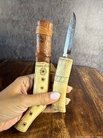 Front view of knife with blade open, showing the inscribed bone or ivory handle with leather strap and carved sheath.