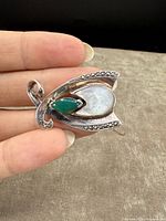 Photo showing the front side of the silver brooch held in hand to display size and details of chrysoprase, mother of pearl, and marcasite stones.