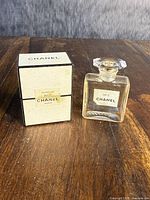 Sealed Chanel No. 5 perfume bottle with original box and empty bottle side by side on wooden surface.