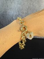 Bracelet worn on wrist showing gold-tone chain links and heart padlock charm with clear stones, photographed from front and side angles.