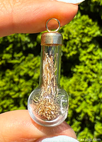 Close-up of the glass bulb pendant held between fingers, showing internal gold shavings and gold cap with loop attachment.