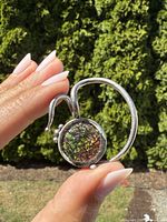 Front side of the pendant held in hand, showing the round ammolite gemstone with iridescent colors and the sterling silver brutalist design.