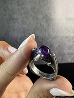 Close-up of the ring showing the sterling silver band with a round amethyst stone held by sculptural prongs, highlighting the brutalist mid-century modern design.