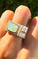 Close-up photo of vintage sterling silver ring on finger, showcasing rectangular natural opal with gold bezel and chunky geometric silver band.