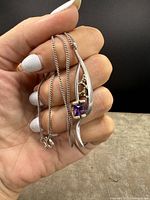 Pendant and chain held in hand showing front view with amethyst and gold accents