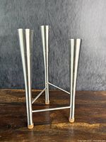 Front side view of the three-arm stainless steel candle holder on a wooden surface with a grey backdrop.