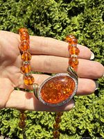 Front view of the pendant showcasing the large oval amber and silver setting against hand and outdoor background