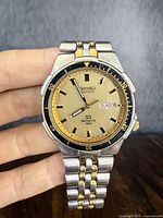 Front view of two-tone watch face showing dial, hands, day-date window and bezel.