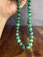 Full view of the graduated malachite bead necklace held in hand showing bead size variation and polished finish.