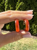 Close-up of both earrings held together showing the red agate hoops under natural light.