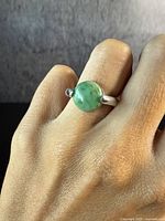 Side view of vintage sterling silver ring with round green jade stone held by bezel setting on finger showing color and texture of jade.