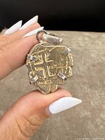 Close-up front view of vintage sterling silver mounted shipwreck-style coin pendant, highlighting the coin's cross pattern and silver prong mounts.