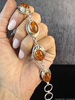 Close-up of bracelet held in hand showing multiple oval amber stones and silver links.