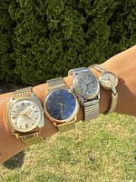 Four vintage wrist watches worn on wrist showing variety in size, dial color and style