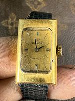 Front view of the Omega De Ville rectangular watch showing worn gold-tone case and gold dial with black markers and hands.
