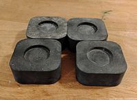 Four black square rubber anti vibration blocks with recessed circle shape on top, shown from above on a wooden surface.